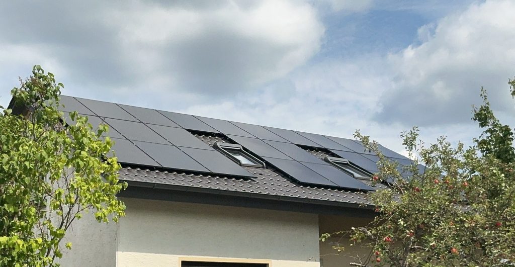 PV-Anlage mit Solarmodulen und Dachfenstern auf einem Hausdach unter bewölktem Himmel.